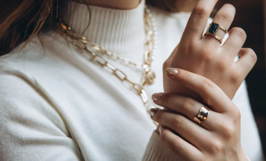 A person wearing a white sweater and gold jewelry

Description automatically generated